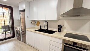 Ett modernt kök med vita skåp, en diskho i rostfritt stål, en ugn från Bosch och ett fönster med utsikt över omgivningen.