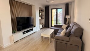 Ett modernt vardagsrum med en platt-TV, en soffa, ett soffbord och ett fönster med gardiner.