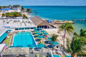 Un resort con una amplia piscina, tumbonas y una zona de playa con sombrillas.