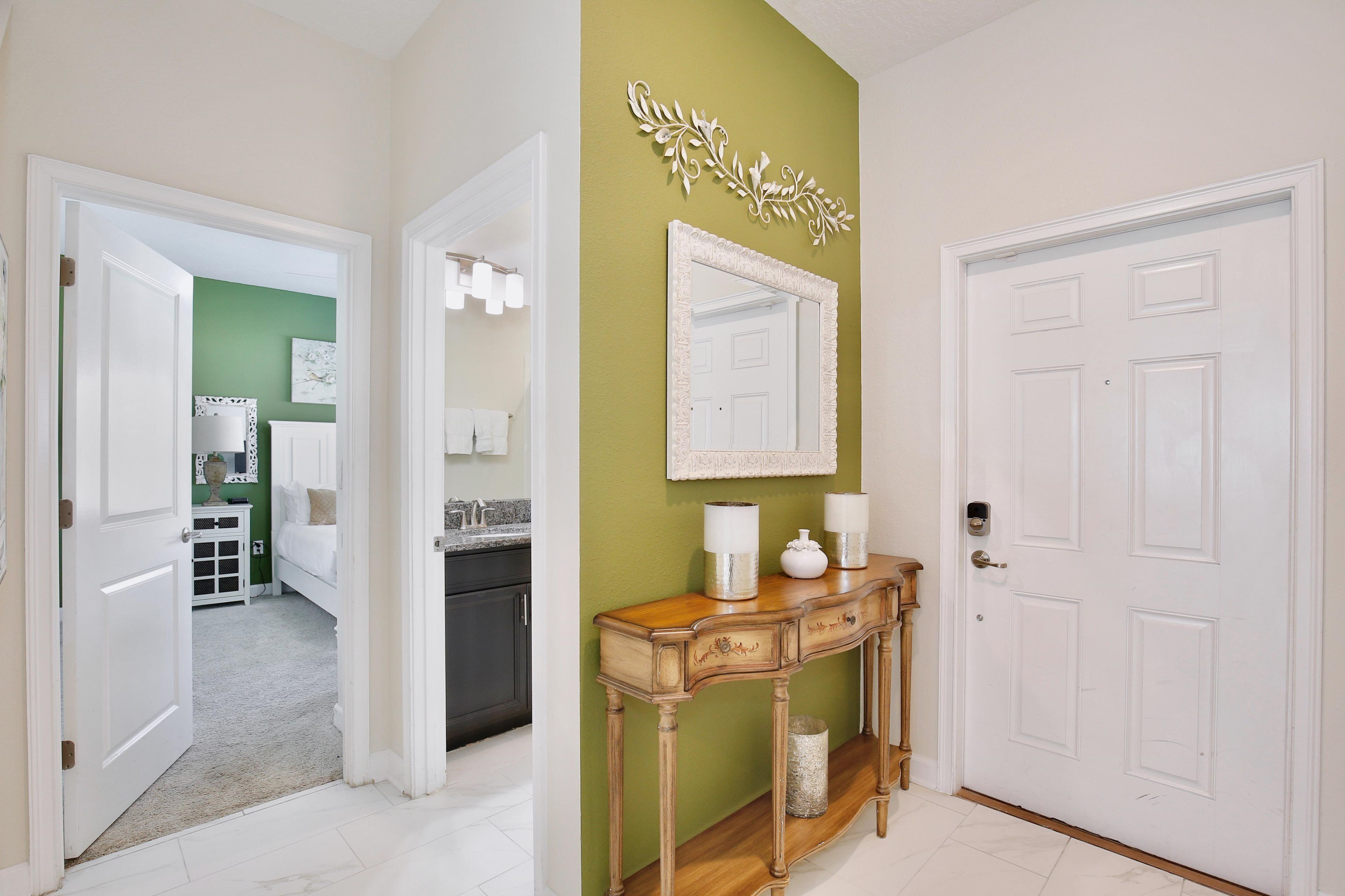 Un couloir avec un mur vert, une porte blanche et une console ornée d’objets décoratifs.