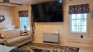 Un salon chaleureux avec un grand téléviseur à écran plat, un canapé, un divan gris et un tapis à motifs.
