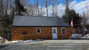 Une cabane en bois avec un toit en métal, une allée en gravier et un drapeau américain.