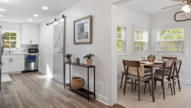 A modern kitchen with white cabinets, a stainless steel refrigerator, and a dining area with a wooden table and chairs. - The Blue Door Bungalow. Walk to Duke Medical/VA. (Durham)