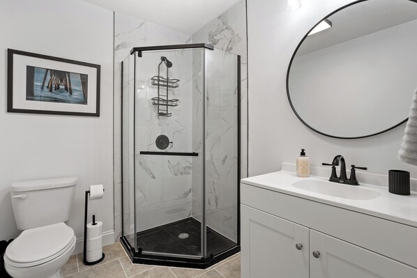 A modern bathroom with a glass-enclosed shower, a toilet, a sink with a mirror, and a framed picture on the wall.