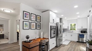 A modern kitchen with white cabinets, stainless steel appliances, and a wooden dining area. - The Blue Door Bungalow. Walk to Duke Medical/VA. (Durham)