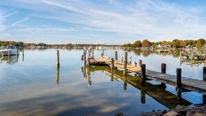 A calm lake with a wooden dock extending into the water, surrounded by trees and buildings in the background. - Sunset Cottage - West River Access and Views! (Shady Side)