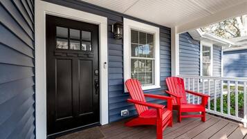 A porch with a black door, a window, and two red Adirondack chairs.