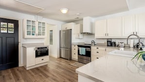 A modern kitchen with white cabinets, stainless steel appliances, and a marble countertop. - Sunset Cottage - West River Access and Views! (Shady Side)