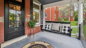 A porch with a black door, a bench with checkered cushions, and a potted plant. - Welcome to Grand Victorian on Main! (Ligonier)