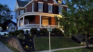 A two-story house with a porch, a well-maintained lawn, and a street sign. - Welcome to Grand Victorian on Main! (Ligonier)