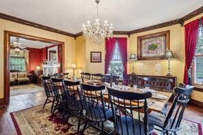 A dining room with a chandelier, red curtains, and a stained glass window.