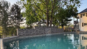 A swimming pool with a stone wall and wooden deck. - Welcome to Grand Victorian on Main! (Ligonier)