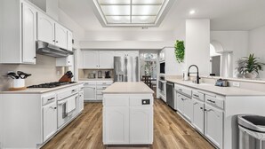Una cucina moderna con mobili bianchi, un'isola centrale e un lucernario.