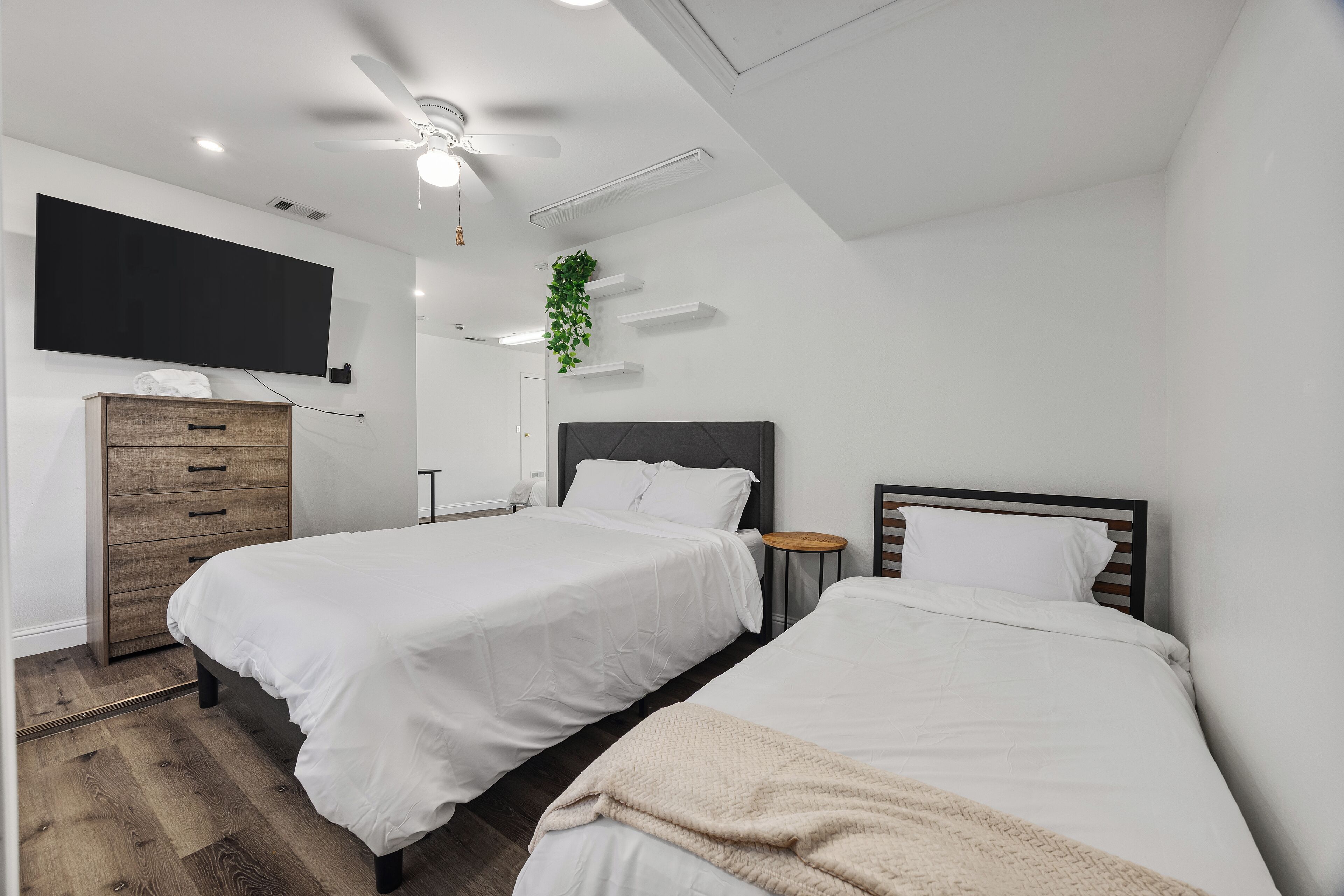 Een moderne slaapkamer met twee bedden, een plafondventilator, een tv aan de muur en een kleine plant.
