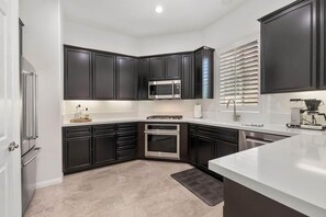 A modern kitchen with dark cabinetry, stainless steel appliances, and a white countertop. - Desert Oasis: Close to Pools, Golf and Coachella! (La Quinta)