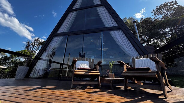 Un moderno edificio de vidrio triangular con una terraza de madera y asientos al aire libre.