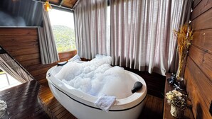 Un cuarto de spa con una bañera de hidromasaje grande, paredes de madera y vistas a la vegetación.