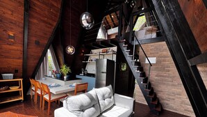 Un acogedor loft con comedor, un sofá, un reposapiés azul y una escalera que lleva a un nivel superior.