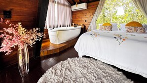 Un dormitorio de cabaña acogedor con interior de madera, una bañera, una alfombra mullida y una ventana con cortinas.