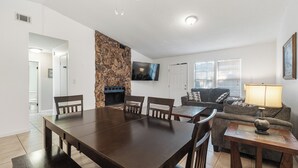 Una sala de estar con una mesa de comedor, sillas, chimenea, televisor, sofá y lámpara.
