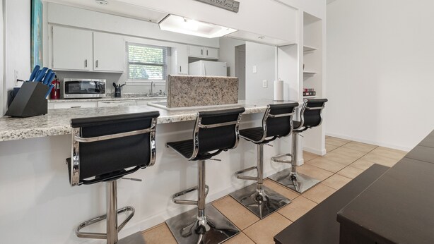 Cocina moderna con armarios blancos, encimera de granito y una zona de bar con tres taburetes.