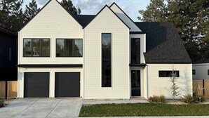 A modern two-story house with a garage, a front yard with landscaping, and a clear sky. - The Nordic Nest on the Greenbelt (Boise)