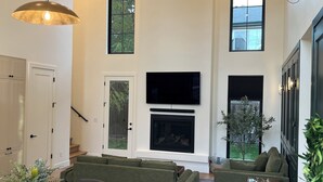 A spacious living room with a fireplace, green sofas, a dining table, and a mounted deer head sculpture. - The Nordic Nest on the Greenbelt (Boise)
