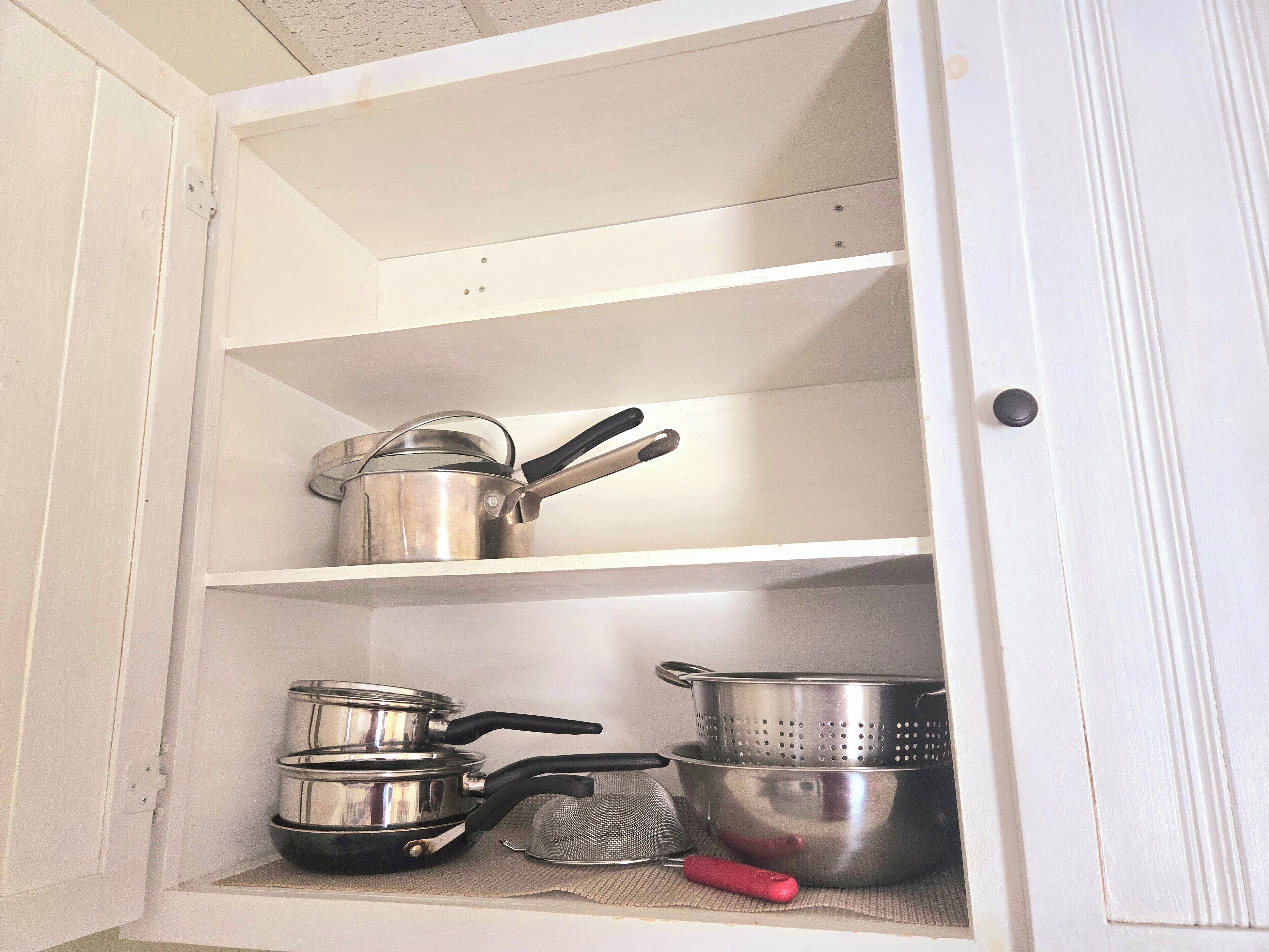 A kitchen cabinet with stainless steel cookware and utensils.