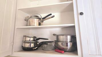 A kitchen cabinet with stainless steel cookware and utensils.