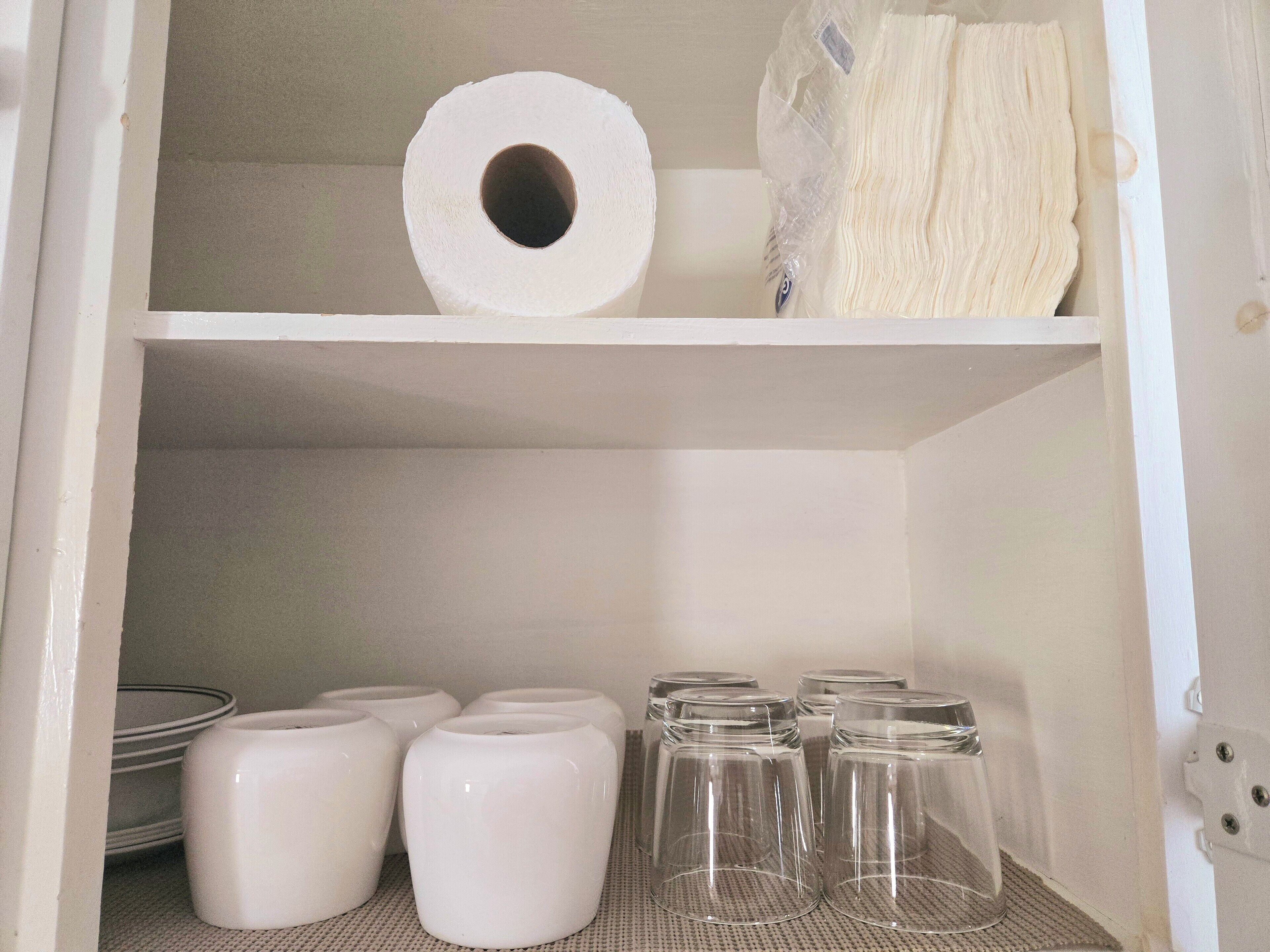 Une étagère avec un rouleau de papier toilette, un paquet de papier toilette et plusieurs bocaux en verre.