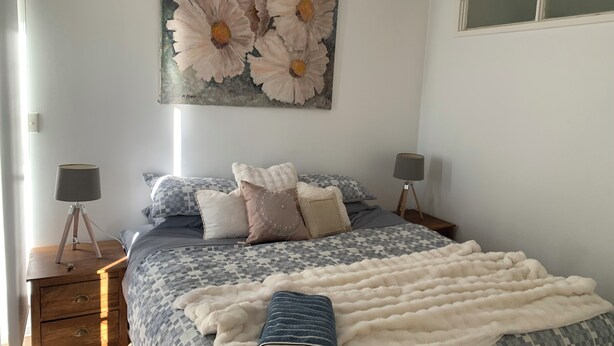 Une chambre à coucher avec un lit, deux tables de chevet, une lampe sur pied et un tableau de fleurs accroché au mur.