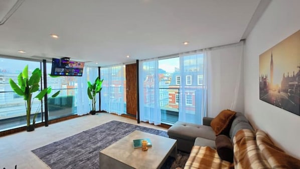 A modern living room with a large window, a flat-screen TV, a sofa, and a coffee table. - Modern Soho Penthouse with Terrace & Views | 3 Beds, Sleeps 6 (London)