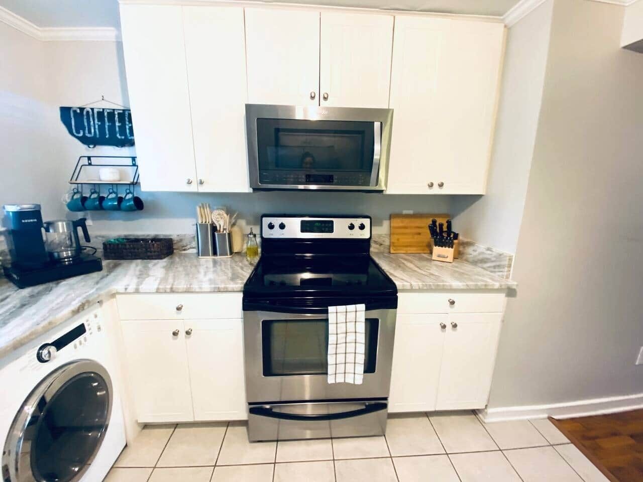 A compact kitchen with white cabinets, a stainless steel oven, a microwave, and a coffee station.