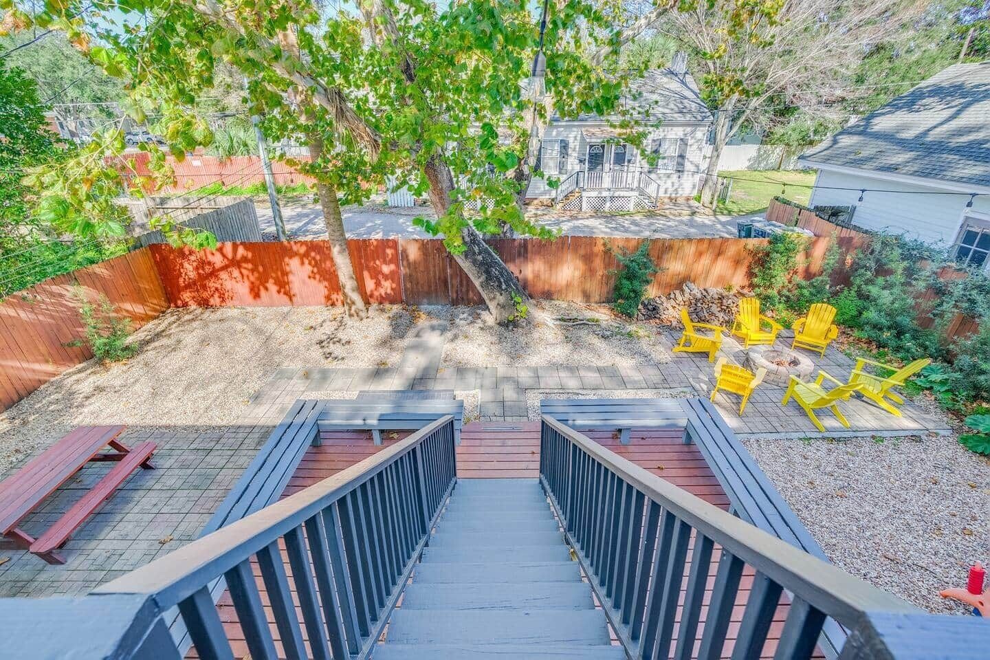 A backyard with a wooden deck, yellow Adirondack chairs, and a small fire pit.