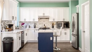 A modern kitchen with white cabinets, a central island, stainless steel appliances, and a teal accent wall. - Lakeview Retreat in Elsinore with Pool & Hot Tub (Lake Elsinore)