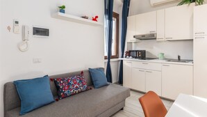Ein modernes Wohnzimmer mit Sofa, Couchtisch und Küchenzeile inklusive Schränken und Geräten.