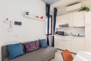 A modern living room with a sofa, a coffee table, and a kitchen area with cabinets and appliances. - Peaceful 1-Bedroom Flat | Steps from Metro (M1) (Milano)