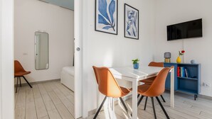 Ein modernes Wohnzimmer mit einem weißen Sofa, orangefarbenen Sesseln, einem weißen Esstisch und einem blauen Bücherregal.