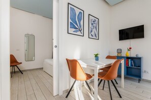 A modern living room with a white sofa, orange chairs, a white dining table, and a blue bookshelf. - Peaceful 1-Bedroom Flat | Steps from Metro (M1) (Milano)