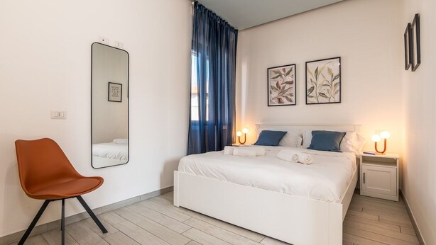 Ein Schlafzimmer mit einem Bett, einem Sessel, einem Nachttisch, einem Spiegel und Bildern an der Wand.