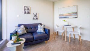 Een moderne woonkamer met een donkerblauwe bank, witte stoelen, een klein rond tafeltje en kunst aan de muren.