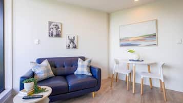 A modern living room with a dark blue sofa, white chairs, a small round table, and artwork on the walls.