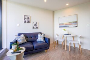 A modern living room with a dark blue sofa, white chairs, a small round table, and artwork on the walls. - Light-Filled Studio with Lovely Ponsonby Views (Auckland Central)