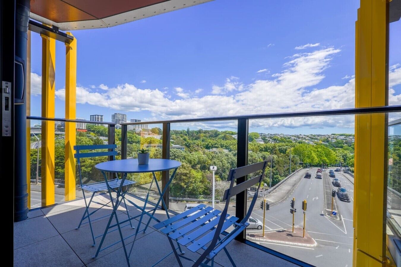 A balcony with a table and chairs, a view of a road, and a clear sky.