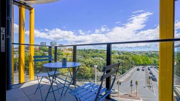 A balcony with a table and chairs, a view of a road, and a clear sky.