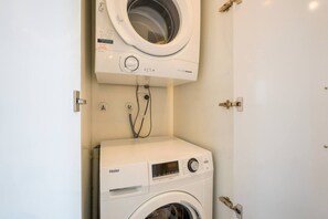 A compact laundry room with a front-loading washer and a top-loading dryer. - Light-Filled Studio with Lovely Ponsonby Views (Auckland Central)