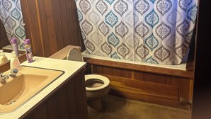 Een badkamer met een houten wastafelmeubel, een toilet en een douchegordijn met een geometrisch patroon.
