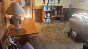 Een gezellige kamer met een houten tafel, een boekenkast, een bank en een deur naar een andere kamer.