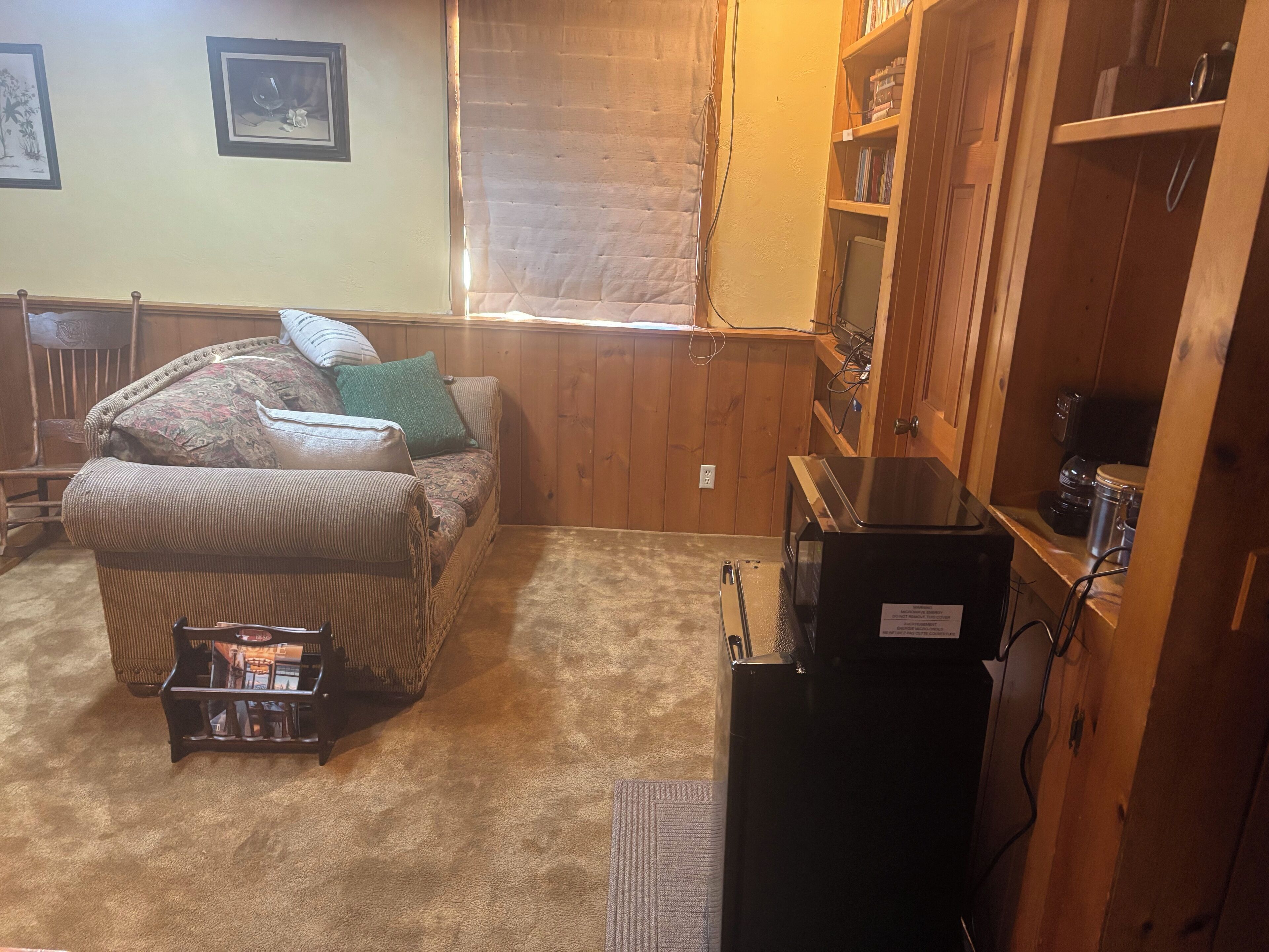 A cozy room with a couch, a small table, a bookshelf, and a refrigerator.