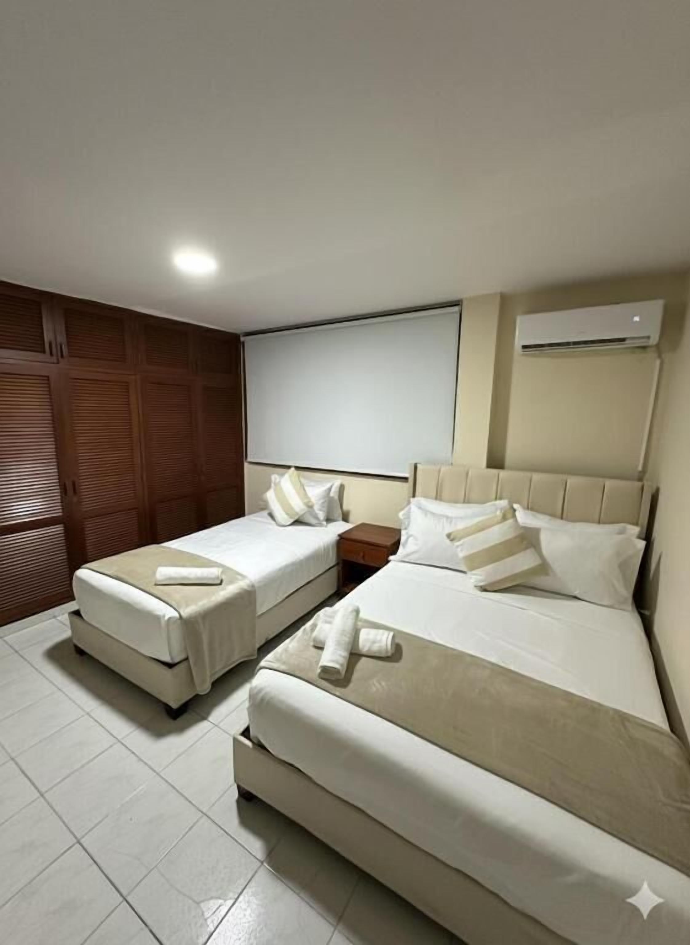 Une chambre d’hôtel avec deux lits, une armoire en bois, une table de chevet et un appareil de climatisation.